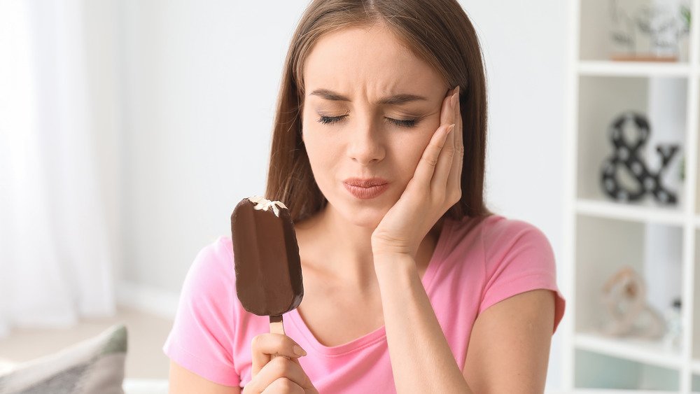 Une femme mangeant une glace se tient la joue de douleur