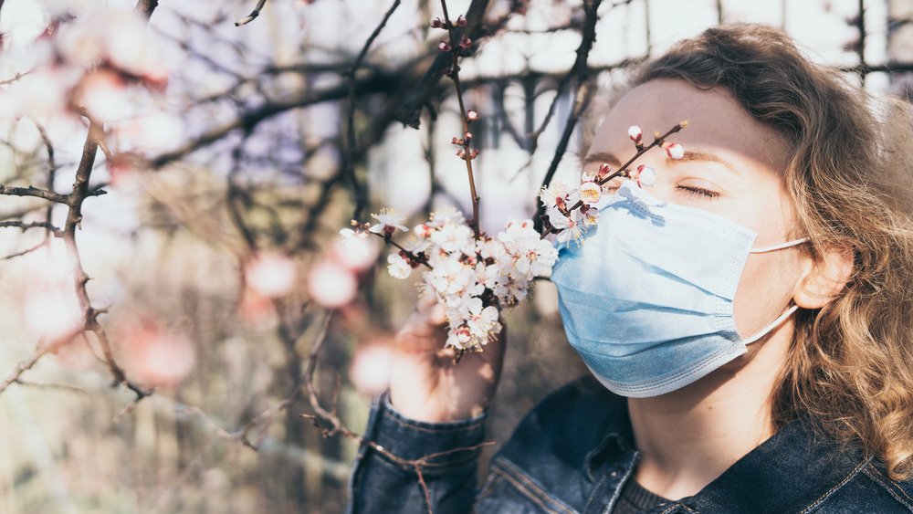 Une femme portant un masque facial renifle les fleurs des arbres