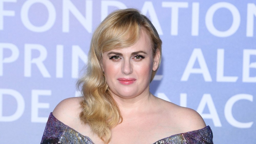 Rebel Wilson souriant dans une robe à épaules dénudées 