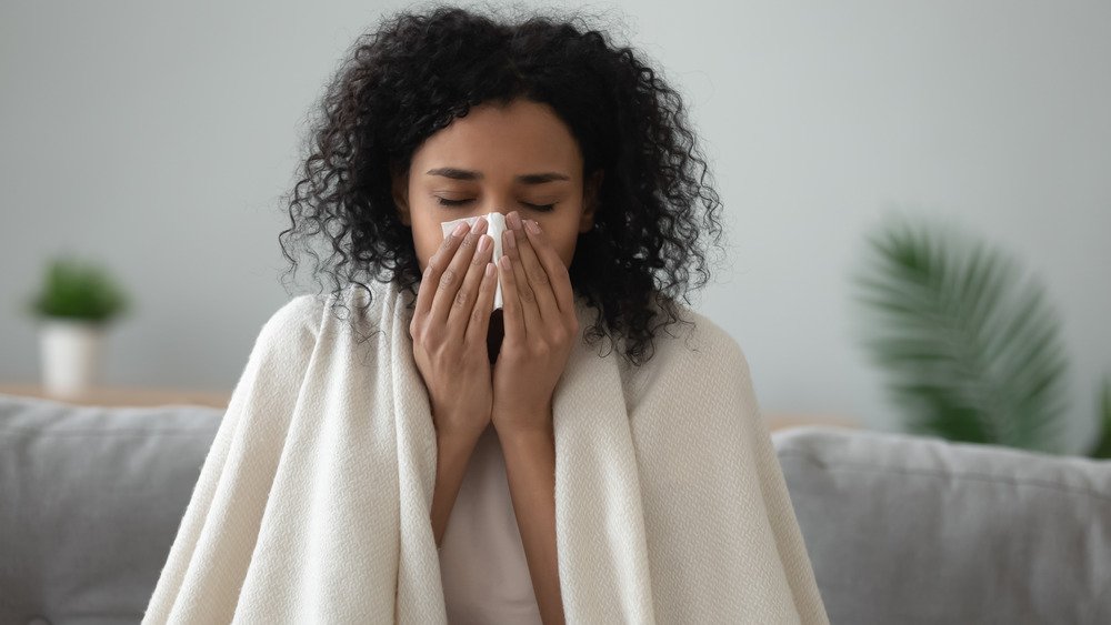 Jeune femme assise sur un canapé dans une couverture se mouchant