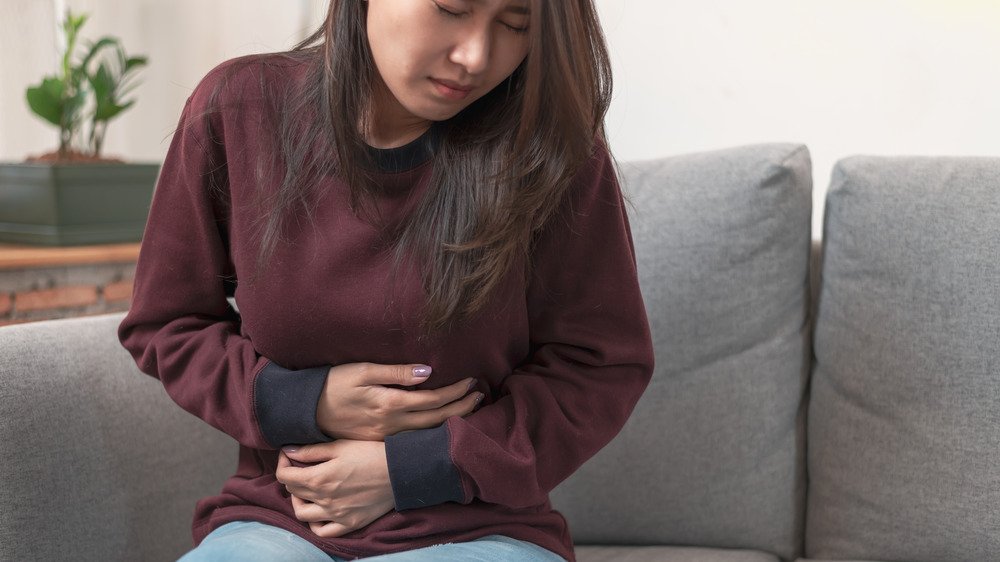 Une femme assise sur un canapé se tenant le ventre en raison de douleurs