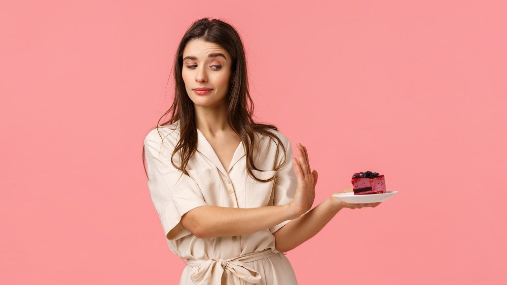 Une femme refusant un gâteau avec un fond tout rose 