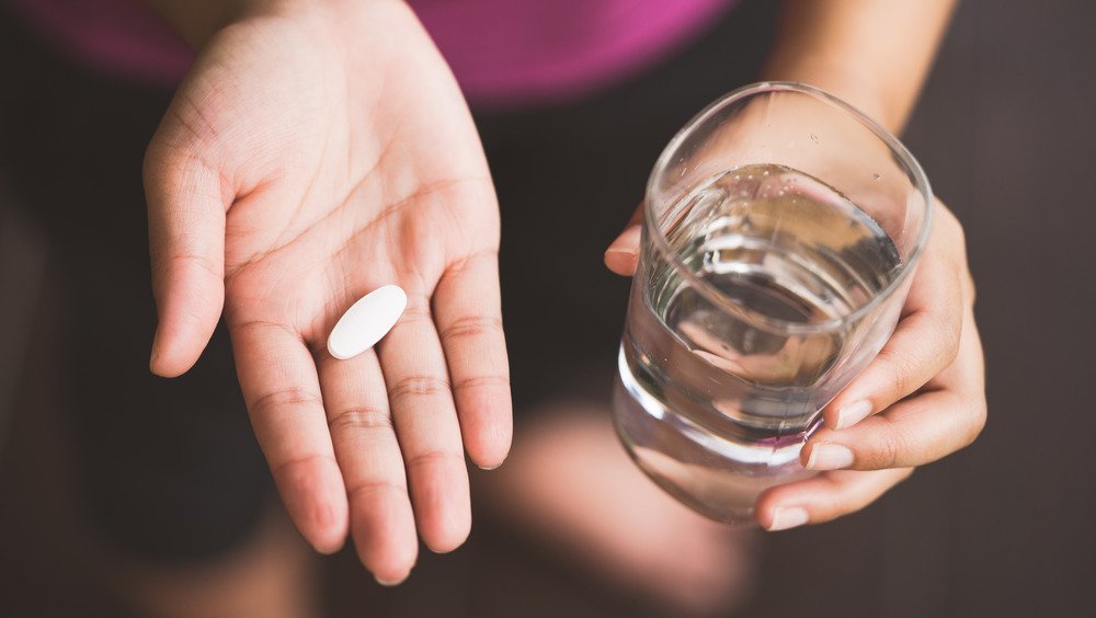 les mains d'une femme tenant une pilule et un verre d'eau