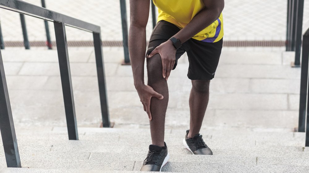 Homme dans un escalier tenant son tibia et son genou