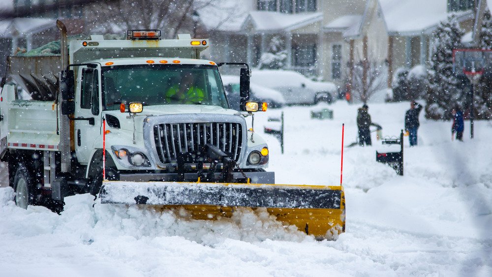 Chasse-neige descendant une route enneigée avec des gens en arrière-plan