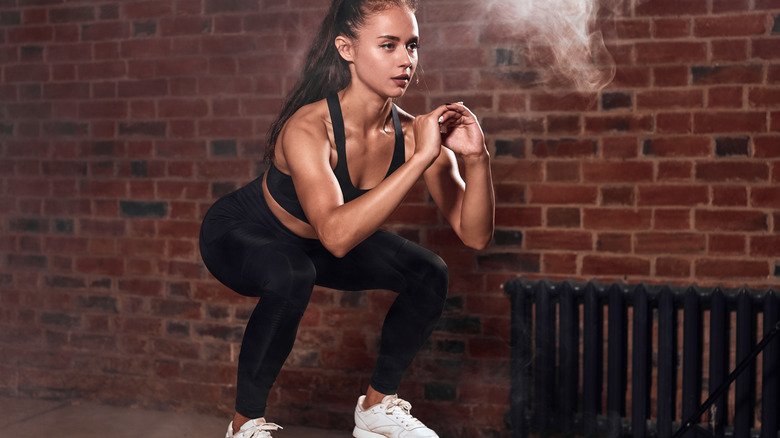 femme accroupie devant un mur de briques