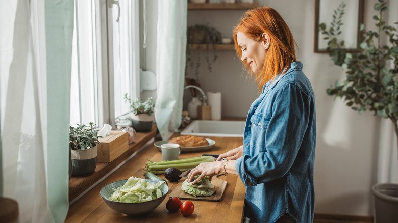 femme aux cheveux roux coupant des légumes