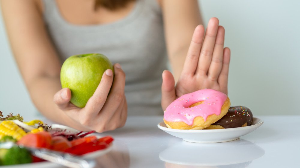 femme tenant une pomme et repoussant des beignets