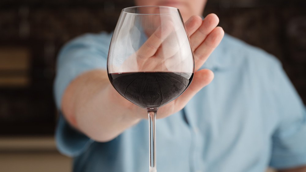 Une personne refuse un verre de vin avec la main levée