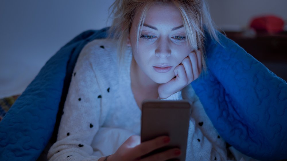 Une femme au lit sous les couvertures regardant son téléphone 