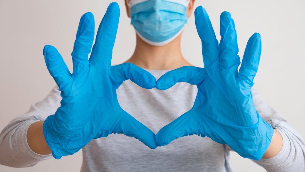 Femme portant un masque médical et des gants faisant un signe de cœur avec les mains