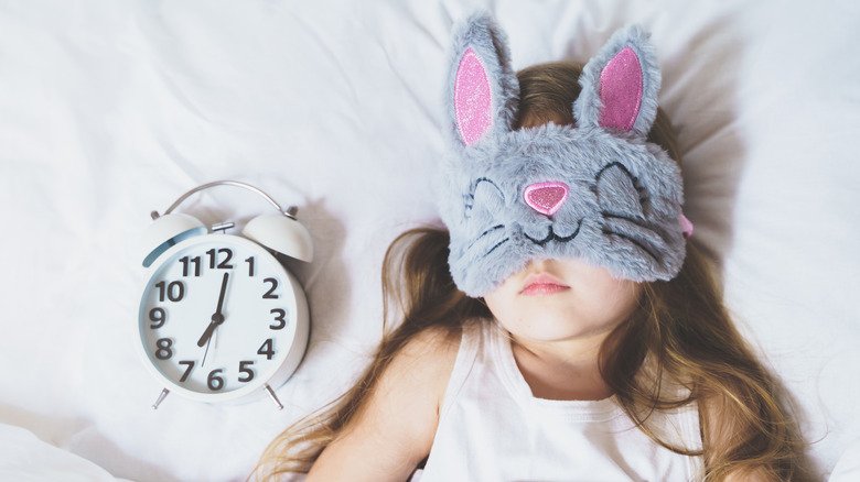 Fille avec un masque de sommeil en forme de lapin, à côté de l'horloge