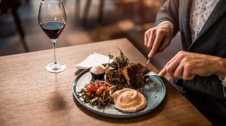 Mains coupant un steak assiette de légumes verre de vin