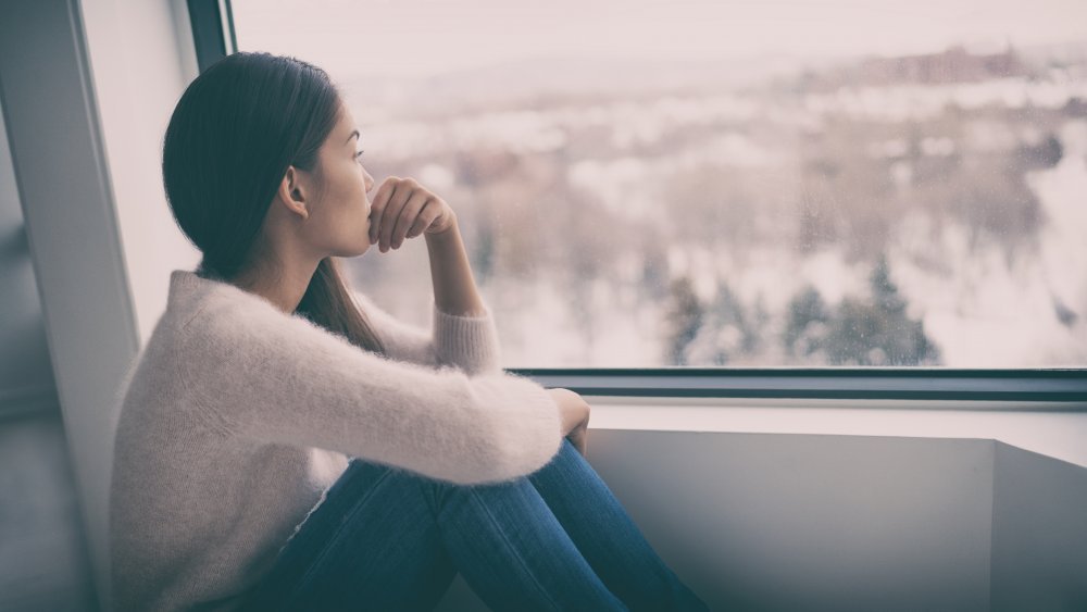 Jeune femme regardant par la fenêtre avec un regard déprimé