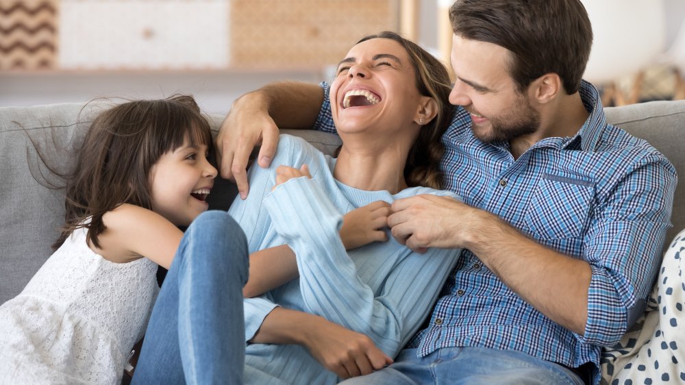 Un père et sa fille chatouillent une mère sur le canapé