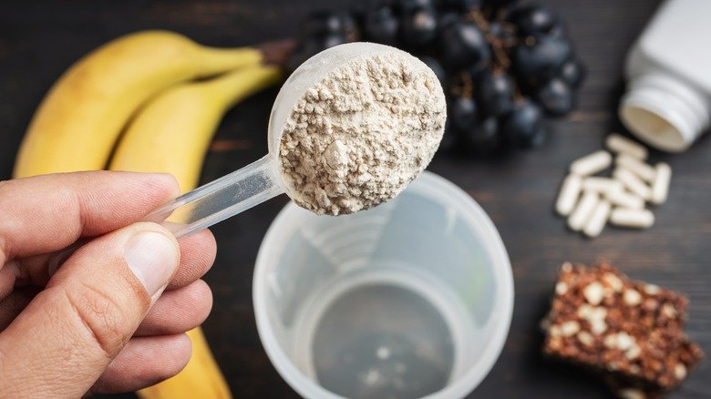 main ajoutant une cuillère de poudre de protéines dans un shaker