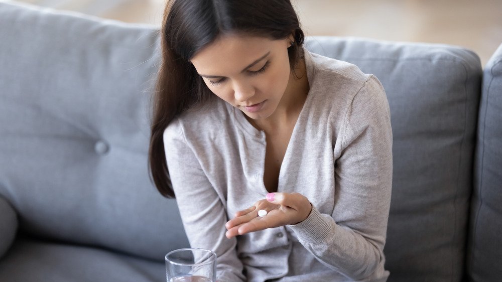 Une jeune femme regarde une pilule dans sa main