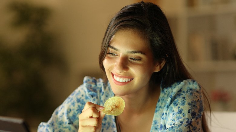 Jeune femme souriante mangeant des chips de pommes de terre